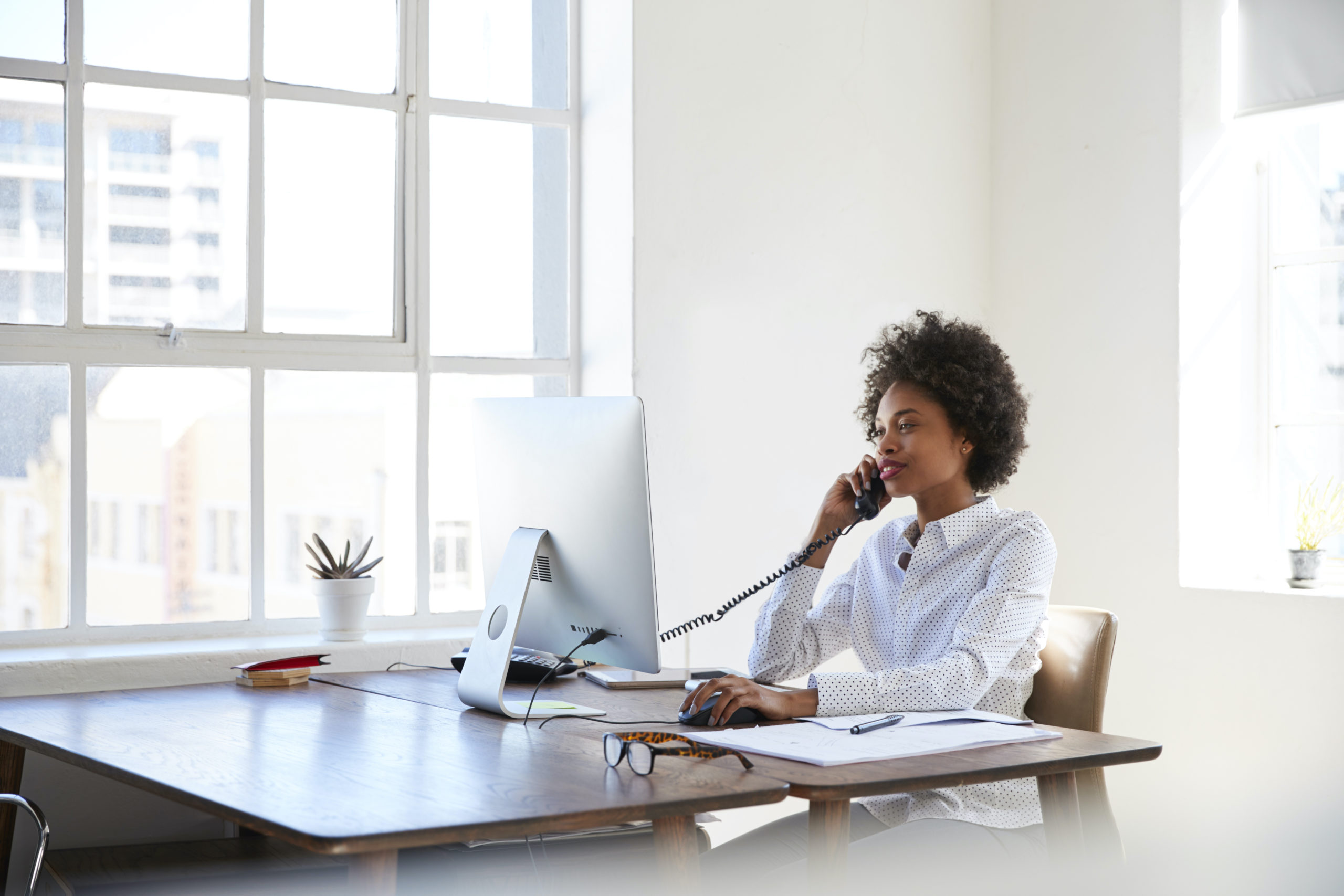Young black woman talking on phone at her desk in an office